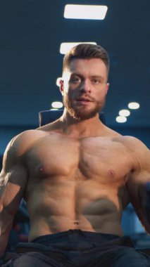 Kaldırma egzersizleri yapan konsantre genç bir atlet. Spor salonunda dambıllı yakışıklı bir sakallı sporcunun portresi. Vücut geliştirici işi. Dikey video