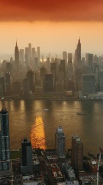 Hudson Nehri 'nin üzerindeki inanılmaz turuncu bulutlar. Günbatımında havadan New York 'un görkemli gökdelenleri. Dikey video