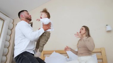 Anne ve baba küçük oğullarını fırlatıyorlar. Yatakta oynayan mutlu anne ve babaya alçaktan bir bakış açısı..