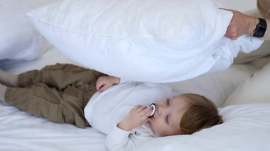 Annesi bebeğinin üzerine emzik emen bir yastık koyuyor. Sevgi dolu anne, sevimli çocuğunu yanağından öper..