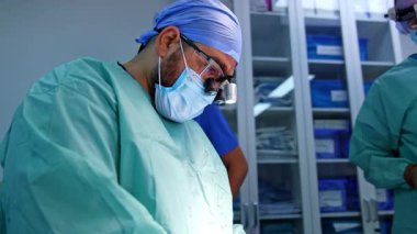 Cerrahi hoparlörlerde sakallı cerrah ameliyat yapıyor. Travma ameliyatında üzerinde kan lekesi olan doktor..