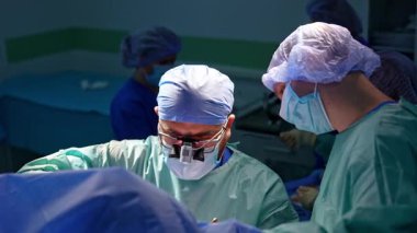 Ortopedist travma operasyonunda çalışıyor. Arkaplanda tıbbi personel doktorlar için araç gereç hazırlar..