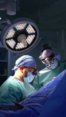 Birkaç cerrah loş ışıkla ameliyathanede çalışıyor. Doktorların arkasındaki tavanda yuvarlak lamba var. Dikey video.