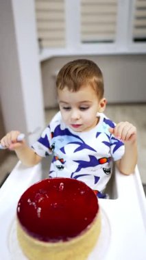 Yüksek sandalyede oturan sevimli çocuk pastayı topluyor. Bebek tatlısını yerken yüksek açılı bir manzara. Dikey video.