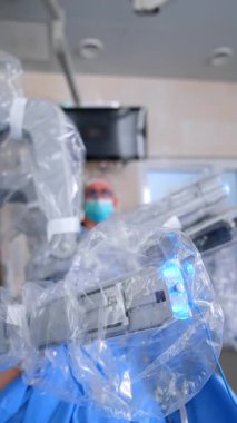 Gelişmiş cerrahın robotik kolları yavaşça hareket ediyor. Da Vinci robotu ameliyat yapıyor. Tanımlanamayan sıhhiyeci arka planda. Dikey video.