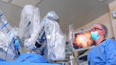 Robot cerrah ve erkek cerrah ameliyatta işbirliği yapıyorlar. Doktor monitördeki operasyonu dikkatlice takip ediyor. Düşük açı görünümü.