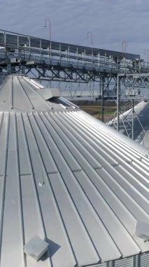 Tahıl asansörlerinin tepeleri. Tahıl depolama ve işleme için modern gümüş ambarlar. Güneş ışığında alüminyum kapların dışı. Havadan bak. Dikey video