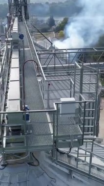 Tahıl asansörlerinin üzerinde metal yapılar var. Tarım fabrikasından gelen zararlı duman havayı kirletiyor. Hava görüntüsü. Dikey video
