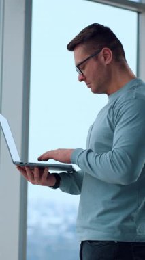 Yakışıklı beyaz adam elinde tuttuğu dizüstü bilgisayara odaklanmış. İş adamının internet üzerinden ortaklarıyla yazışması. Dikey video