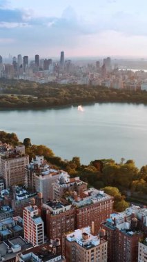 Central Park, New York 'taki su deposunun pürüzsüz yüzeyi. Muhteşem şehir manzarası ve gün batımında yeşil alan. Dikey video