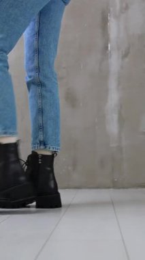 Şık, siyah deri, alçak çizmeli, bağcıklı bir bayan. Kapatın. Kot pantolon giyen bir manken modern ayakkabılarını göstermek için stüdyonun önünden geçiyor. Dikey video
