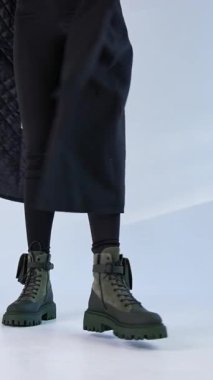 Siyah ceketli kız traktör tabanlı modern çizmelerini sunuyor. Stüdyo ayakkabıları tanıtımı. Dikey video
