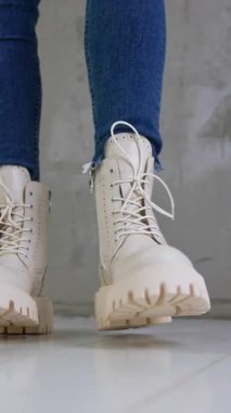 Büyük tabanlı ve bağcıklı yeni süt beyazı asker botları. Kotlu manken kameraya yakın yürüyor ve farklı taraflardan ayakkabıları gösteriyor. Düşük açı. Dikey video