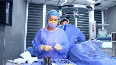 Cerrahi standında sarı gözlüklü beyaz önlüklü hemşire duruyor. Tıbbi uzman operasyon için araç ve materyal hazırlar.