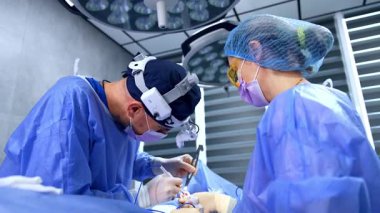Kafkas cerrahı estetik ameliyat yapmak için tıbbi aletler ve aletler kullanıyor. Bir ameliyat hemşiresinin yardımıyla göğüs büyütme ameliyatı yapan bir doktor. Düşük açı görünümü.