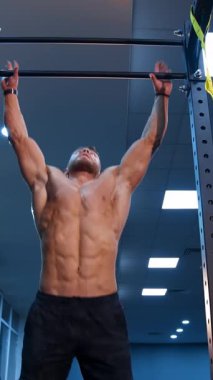 Üstsüz adam yatay çubuğa yanaşıyor. Uyumlu sporcu yatay çubukta karın kası egzersizi yapıyor.