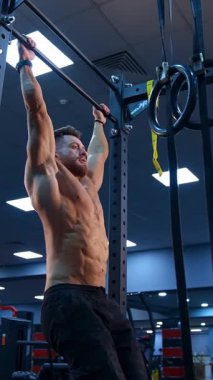 Vücut geliştirici yatay çubukta egzersiz yapıyor. Üstsüz adam spor salonunda yatay çubuğa yanaşıyor.