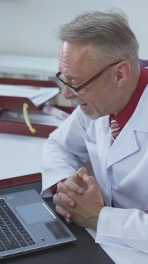 Ofis masasında çalışan erkek doktor. Doktor terapist hasta görüntülü sohbetini klinikteki dizüstü bilgisayarla yapıyor.