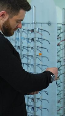 Yeni gözlük deneyen bir adam. Gözlükçülerin perakende dükkanında yeni gözlükleri kontrol eden genç adam