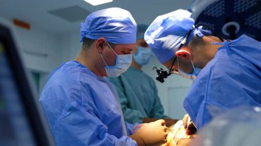 Erkek cerrahlar ameliyata başlayarak hastanın derisini kesiyorlar. Doktorlar modern tıbbi aletleri dikkatli bir şekilde uyguluyorlar..