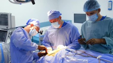 Modern ameliyathanede nöroşirürjide üç doktor çalışıyor. Erkek hemşire aletleri temizler ve baş cerraha verir..
