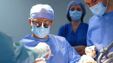 Cerrahi hoparlör takan erkek beyin cerrahı ameliyat masasına oturur. Doktora neşter veriliyor ve kesmeye başlıyor..