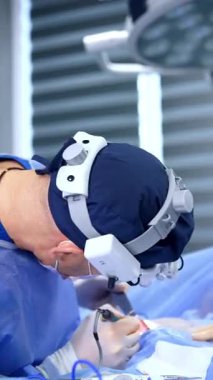 Cerrahi hoparlörlerdeki erkek estetik cerrah modern sihirli aletler ve aletler kullanıyor. Göğüs büyütme ameliyatı yapan doktorun yan görüntüsü. Dikey video.
