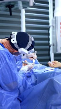 Doktor ameliyatta elektrikli makas aleti kullanır ve ameliyat hemşiresine verir. Erkek cerrah göğüs büyütme ameliyatı yapıyor. Dikey video.