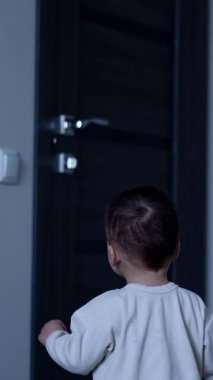 Küçük çocuk ışık düğmesine doğru yürüyor. Bebek sevinçle tezahürat yapıp gülümsüyor. Dikey video