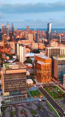Philadelphia 'nın merkezindeki binalar batan güneşin altında. Merkezinde gökdelen kompleksi olan şehrin parlak manzarası. Üst Manzara. Dikey video