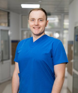 Happy doctor in a hospital. A healthcare worker wearing blue scrubs stands confidently in a hospital corridor, ready to assist patients. clipart