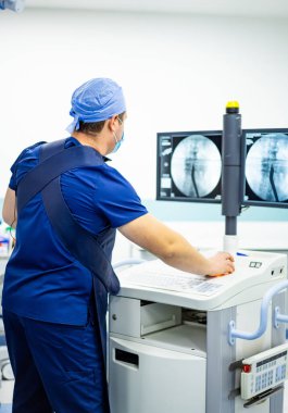 Doktor görüntüleme ekipmanı kullanıyor. Mavi önlüklü bir tıp uzmanı, görüntüleme ekipmanlarını klinik ortamdaki görüntülere bakarken ayarlar..