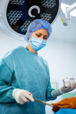 Hassas ameliyatta bir cerrah. Önlük ve maske takan bir tıp uzmanı parlak ameliyathane ışıkları altında cerrahi bir prosedüre odaklanır..