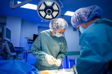 Steril cerrahlar. Cerrahi giyimli cerrahlar modern bir ameliyathanede parlak ışıklar altında dikkatlice bir prosedür uygularlar..