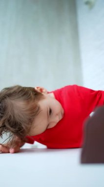 Saçları dağınık beyaz bir erkek bebek masada duruyor. Çocuk masanın üzerinde oyuncaklarıyla oynuyor. Düşük açı. Dikey video.