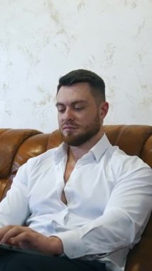 Kanepede otururken dizüstü bilgisayar kullanan Freelancer. Yorgun iş adamı iş gezisinde internette çalışıyor. Otel odasındaki kanepede dinlenen adam. İş rahatlatıcı konsept. Dikey video