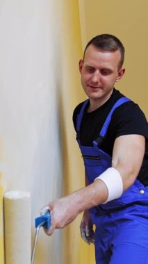 Harekete geçmiş bir ressamın portresi. Dairesinde boya silindiri olan mavi tulumlu bir dekoratör. Oda makyajı. Dikey video