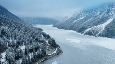 Beyaz donmuş göl muhteşem kayaların arasında. Karlı çam ağaçları dağ yamaçlarını kaplar. Hava görünümü.