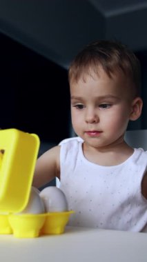 Beyaz erkek bebek oyuncak yumurtalarla oynuyor. Sevimli çocuk kutuyu açar ve kapatır. Kapatın. Dikey video
