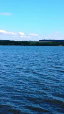 Nehri geçip, rıhtıma kadar takip ediyorum. Doğada güneşli bir gün. Nehir kıyısında yeşil ağaçlar var. Dikey video