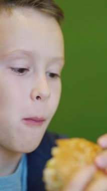 Restoranda hamburger yiyen aç bir çocuk. Fast food kafe. Zararlı beslenme Dikey video