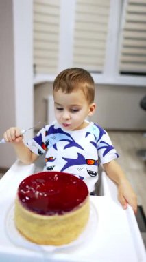 Güzel erkek bebek bir bataklık pastasının önünde yüksek sandalyede oturuyor. Tatlı yiyen çocuğa yüksek açılı bir bakış açısı. Dikey video.