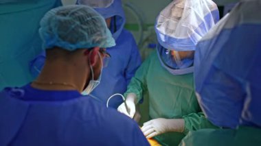 Bir grup cerrah ortopedik ameliyat yapıyor. Kasklı doktor elektrikli alet takıyor. Travma operasyonu.