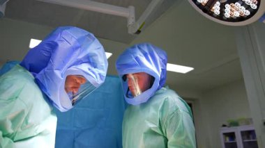 Operasyonda koruyucu kask takan iki beyaz erkek cerrah. Travma ameliyatında metal aletler kullanan doktorlara düşük açılı bakış açısı.