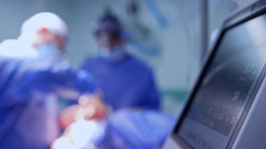 Ciğer havalandırma makinesinin monitörünün yanındaki görüntü. Tıbbi ekip bulanık arkaplanda ameliyat masasında çalışıyor..