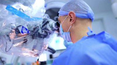 Mikroskop başında oturan cerrah operasyonda konuşuyor. Beyin cerrahı işte elektrikli cihaz kullanıyor.