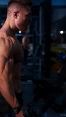 Kas geliştirici Adam Dambılları Tutuyor. Spor salonunda çalışırken dambıl tutan zinde bir genç. Dikey video
