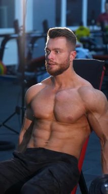 Dambıl tutan genç bir vücut geliştirici. Spor salonunda halterli kaslı adam eğitimi. Dikey video