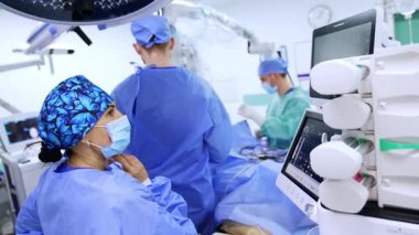 Akciğer havalandırma makinesinin başında duran kadın doktor monitörlere bakıyor. Nöroşirürji ekibi ameliyat masasında çalışıyor..