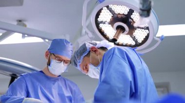 Kafkasyalı doktor ve erkek asistan operasyonda çalışıyor. Cerrahın parlak yuvarlak lambanın altında çalışmasına düşük açılı bakış açısı.